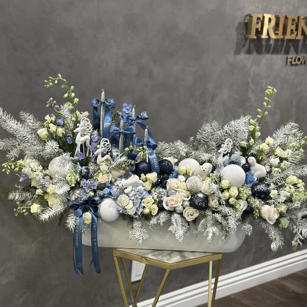Large white floral arrangement with blue ribbons and ornaments in a white container