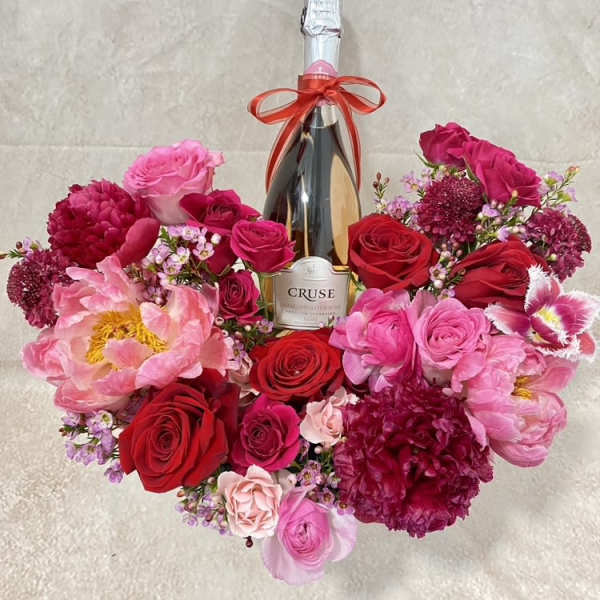 Heart-shaped bouquet of pink and red flowers around a champagne bottle