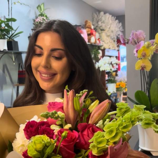 Woman holding a colorful bouquet of roses, lilies, and green blooms
