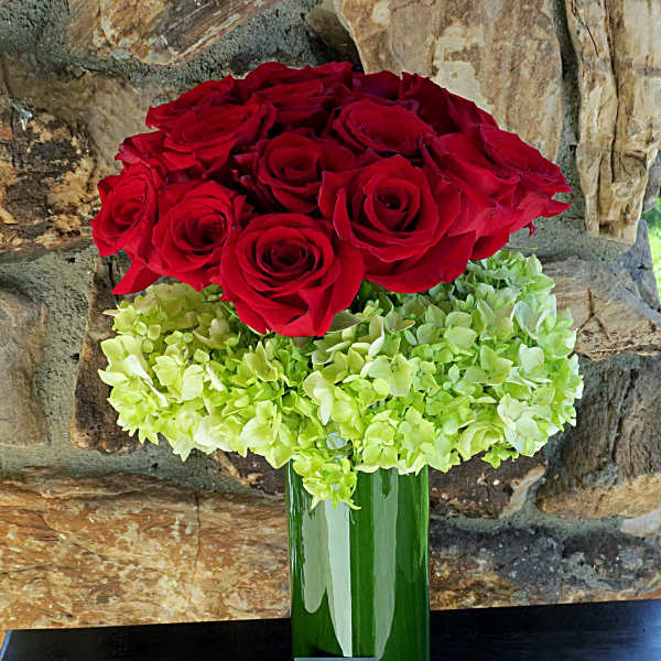 Red roses above a green hydrangea cluster in a tall glass vase