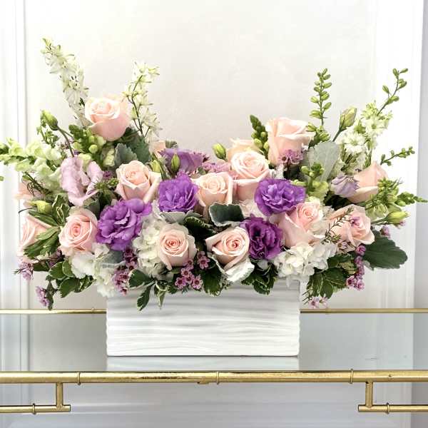 Pink roses and purple blooms arranged in a white rectangular vase