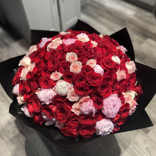 Large round bouquet of red and pink roses with pink peonies wrapped in black paper