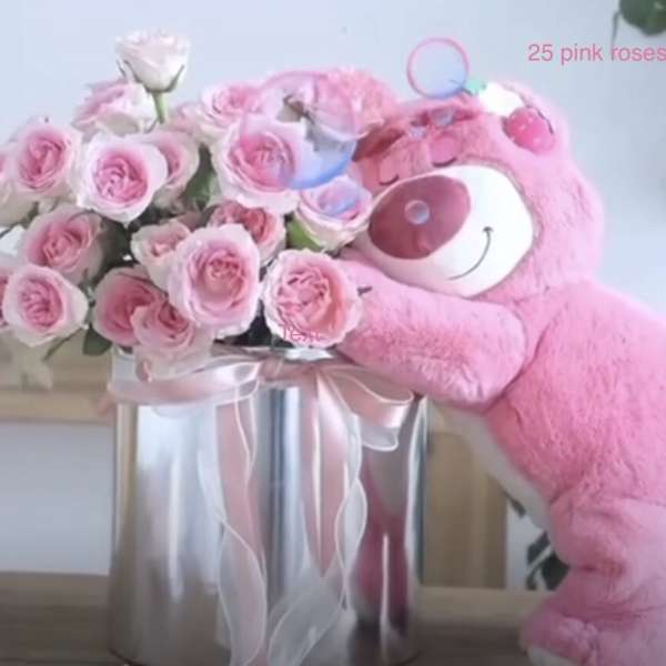 Pink roses arranged in a silver box beside a pink plush bear.