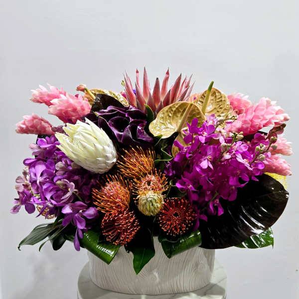 Tropical floral arrangement with pink, purple, and gold blooms in a white vase