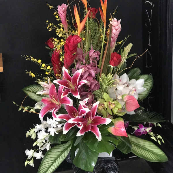 Tall tropical floral arrangement with pink lilies and orchids in a vase