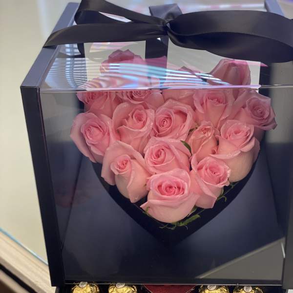 Pink roses arranged in a heart-shaped gift box with chocolates below