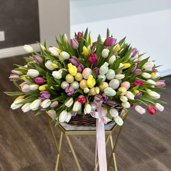 Basket of multicolored tulips with pastel Easter eggs and a pink ribbon