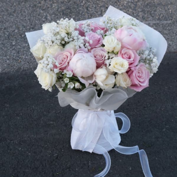 Bouquet of pink and white roses with baby's breath, wrapped in white paper and ribbon