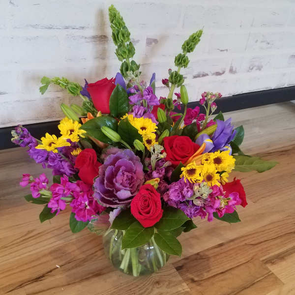 Mixed bouquet of red roses, purple flowers, and yellow daisies in a glass vase