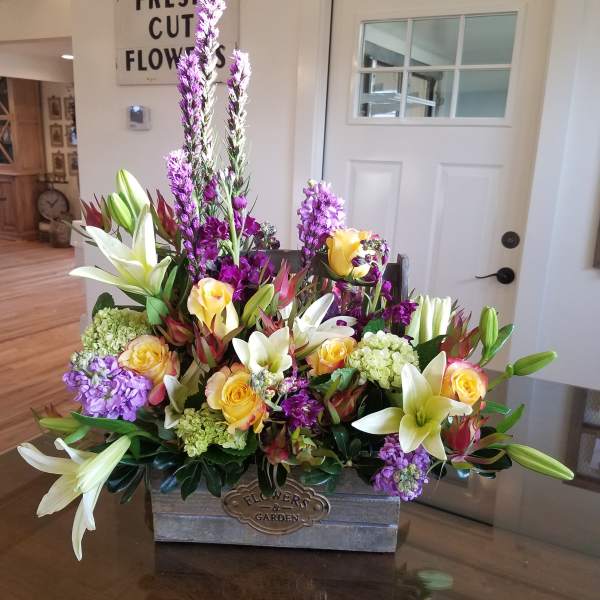 Mixed bouquet of lilies, roses, and purple flowers in a wooden box