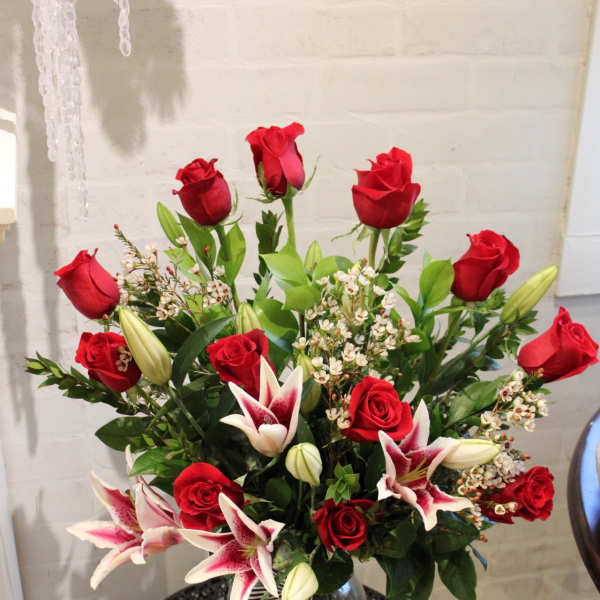 Red roses and pink lilies arranged in a glass vase with a striped ribbon.