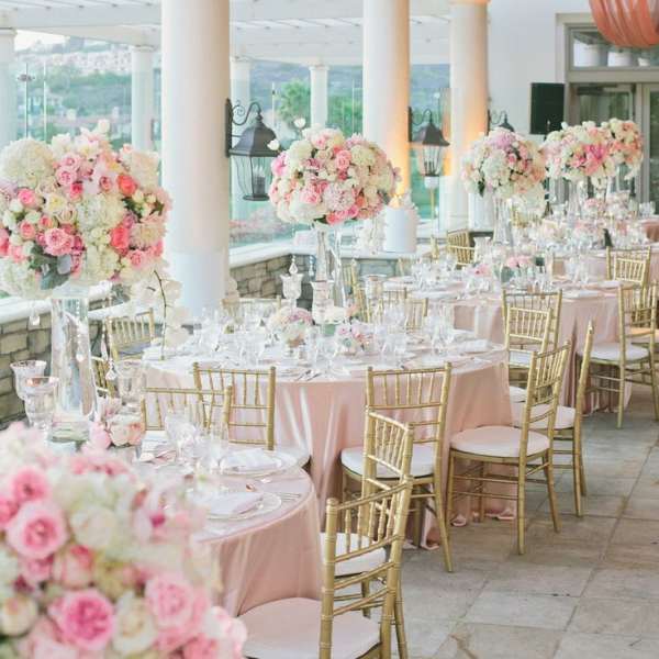 Pink and white floral centerpieces on round banquet tables with gold chairs