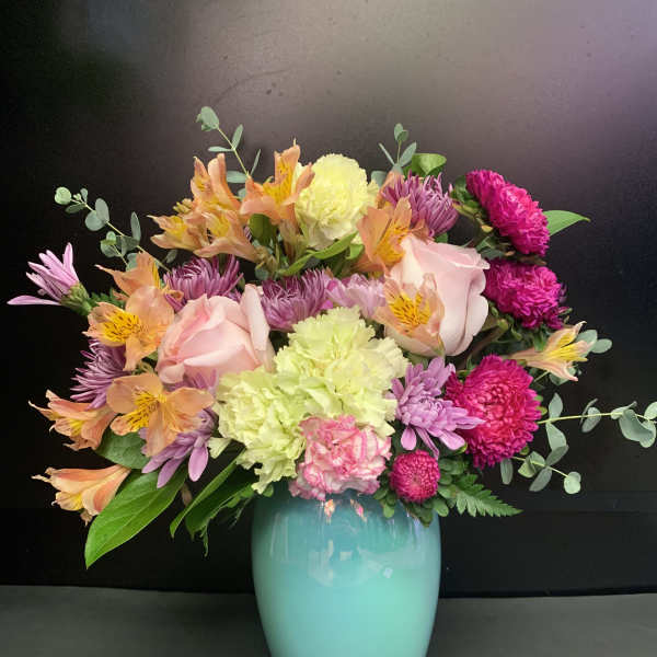 Mixed bouquet in a turquoise vase with pink, purple, and peach blooms