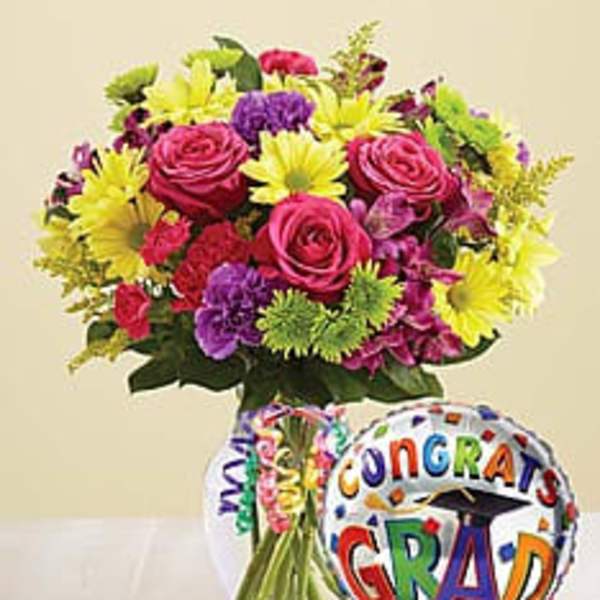Bright mixed bouquet in a glass vase with a colorful Congrats Grad balloon