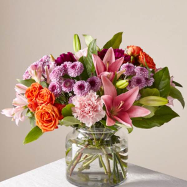 Bouquet of pink lilies, orange roses, and purple flowers in a glass vase