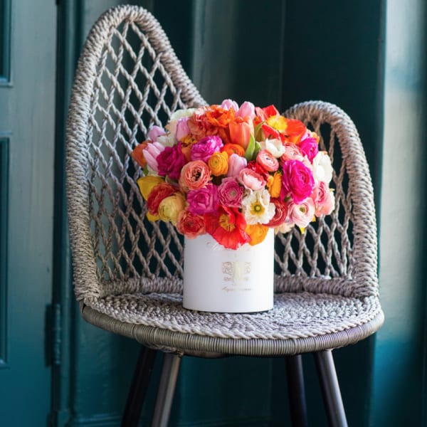 Bright mixed bouquet in a white cylindrical box on a woven chair