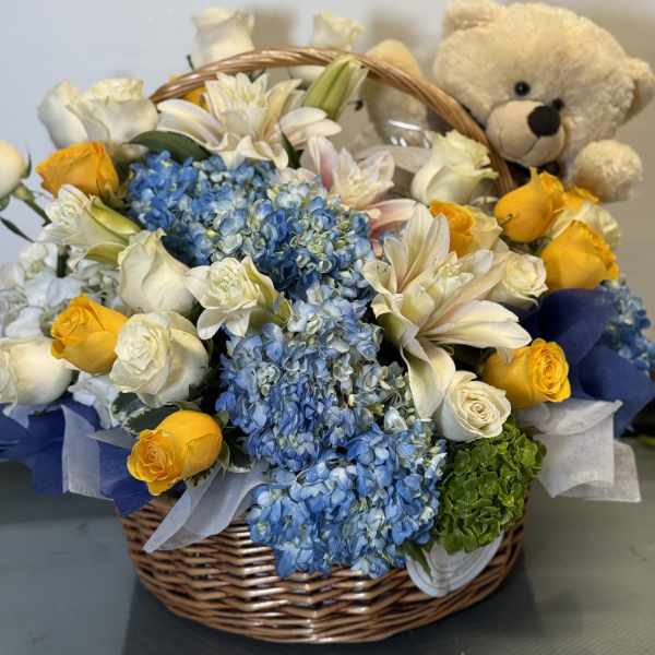 Basket of blue hydrangeas, white roses, yellow roses, and a teddy bear