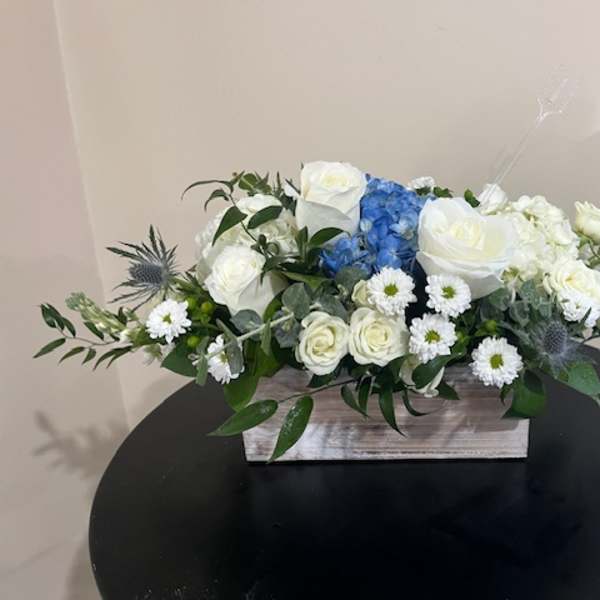 Low white and blue flower arrangement with roses and hydrangea in a rectangular wooden box