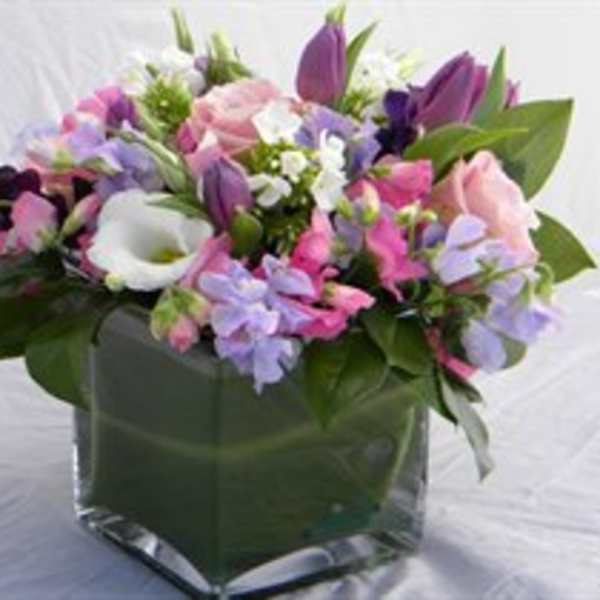 Mixed pink, purple, and white flowers in a square glass vase