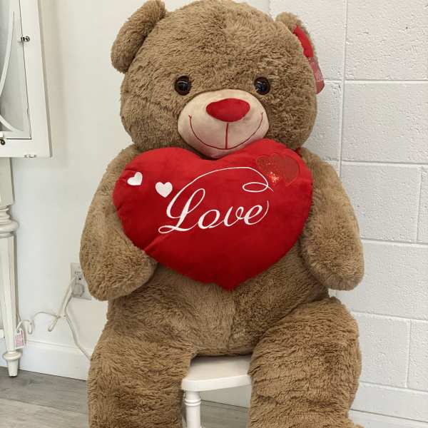 Large teddy bear holding a red heart pillow with the word Love