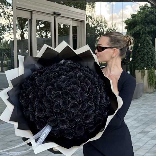 Woman holding a large bouquet of black roses wrapped in black and white paper