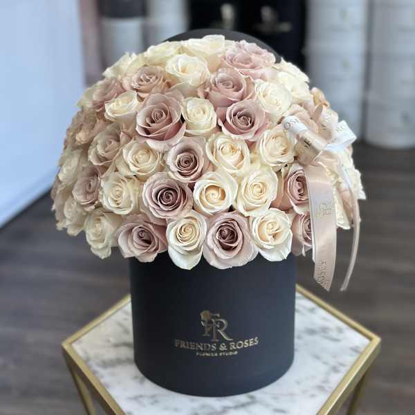 Round bouquet of blush and ivory roses in a black hat box.