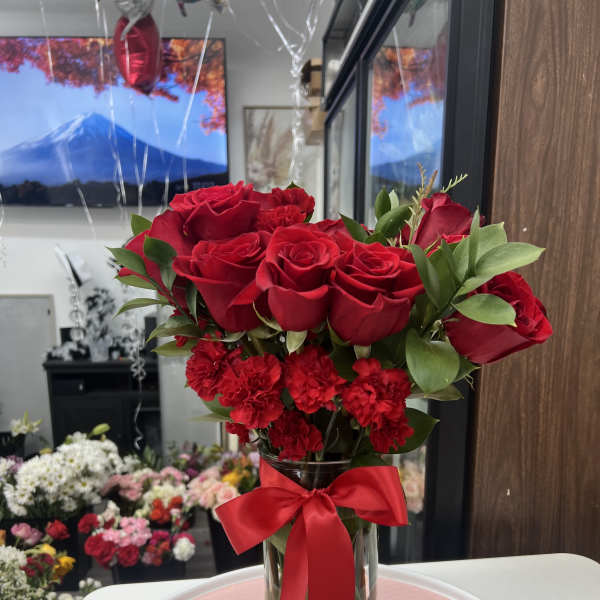 Red roses and carnations in a clear glass vase with a red ribbon.