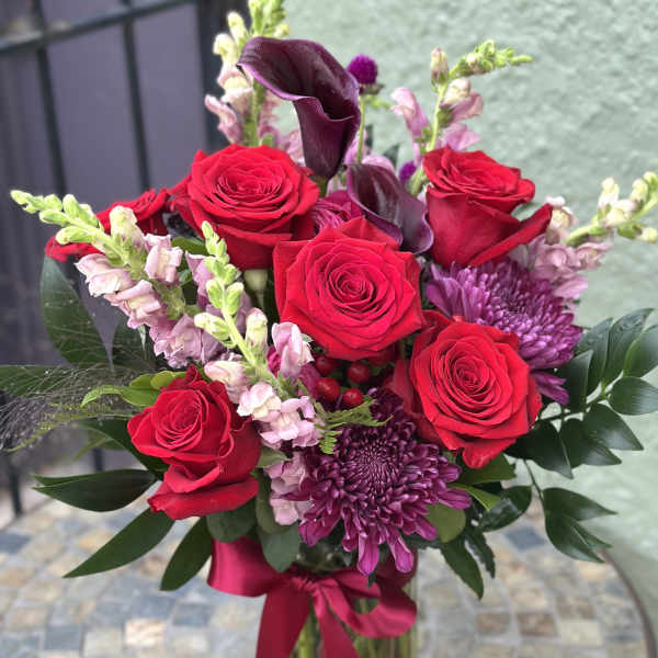 Bouquet of red roses and purple flowers in a glass vase with a ribbon