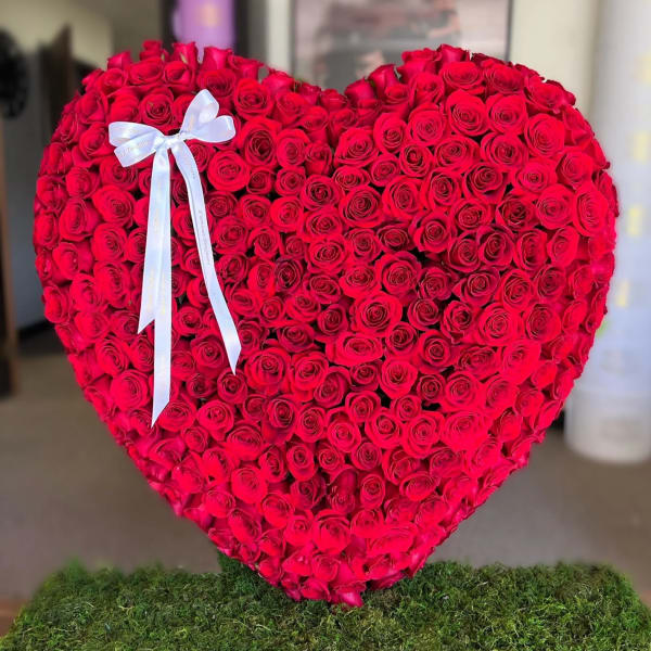 Heart-shaped arrangement of red roses with a white ribbon bow