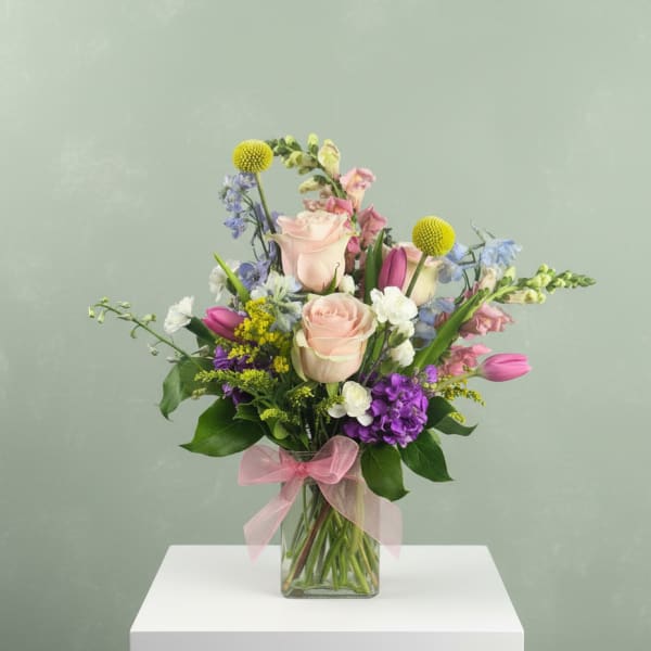 Mixed bouquet of pastel roses, tulips, and purple flowers in a glass vase