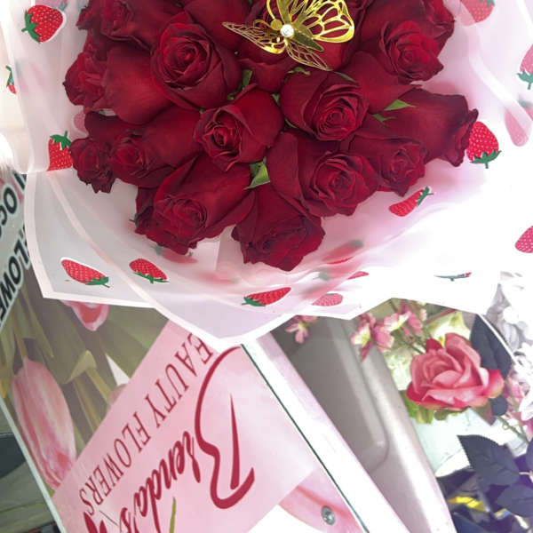 Bouquet of red roses wrapped in strawberry-patterned paper with a gold butterfly pick