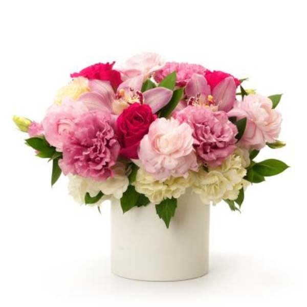 Low pink and white arrangement with roses, carnations, and orchids in a white cylinder vase