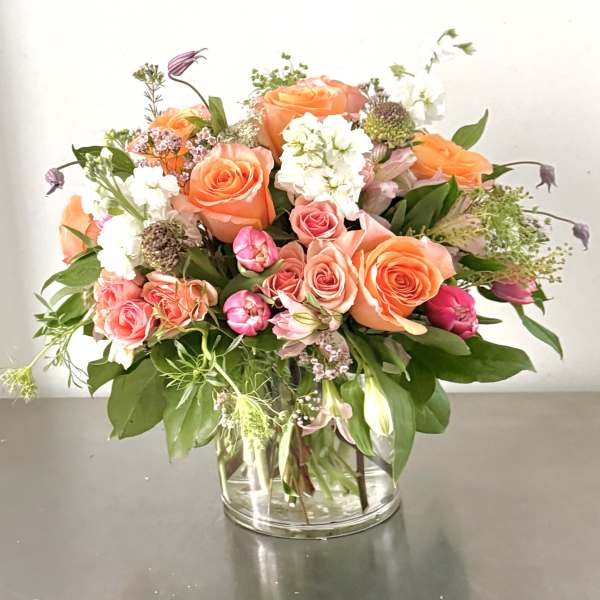 Mixed bouquet of orange and pink roses in a clear glass vase