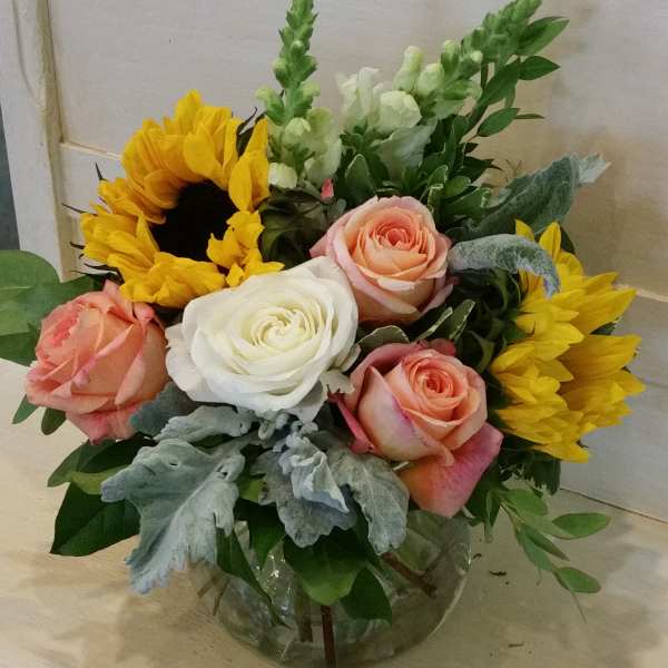 Mixed bouquet with roses, sunflowers, and snapdragons in a glass vase