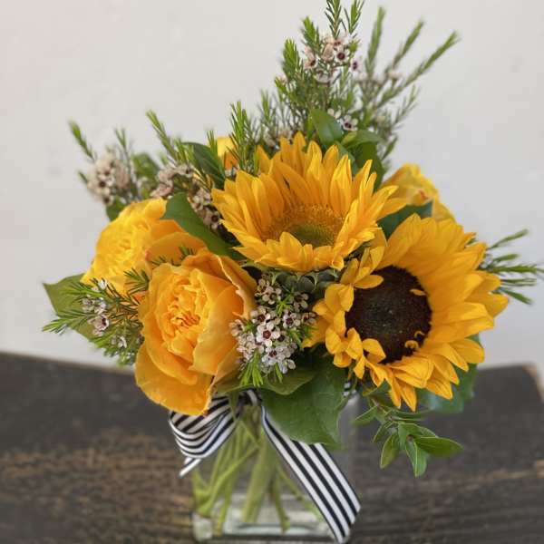 Yellow sunflower and rose bouquet in a glass vase with a striped ribbon