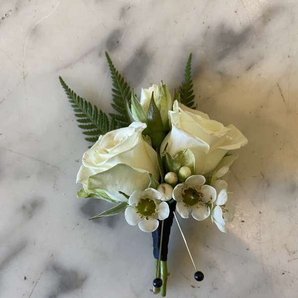 White rose boutonniere with small white accent flowers and fern fronds