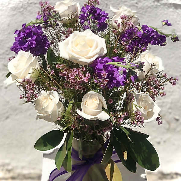 White roses and purple flowers arranged in a glass vase with ribbon