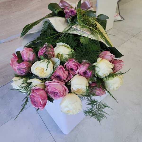 Low arrangement of pink and cream roses in a white square container with a decorative bow.
