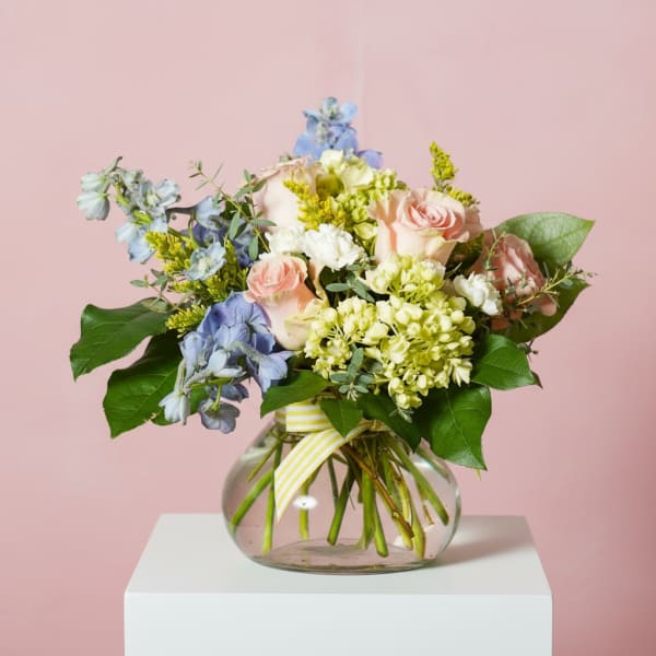 Mixed pastel bouquet in a round glass vase with a striped ribbon