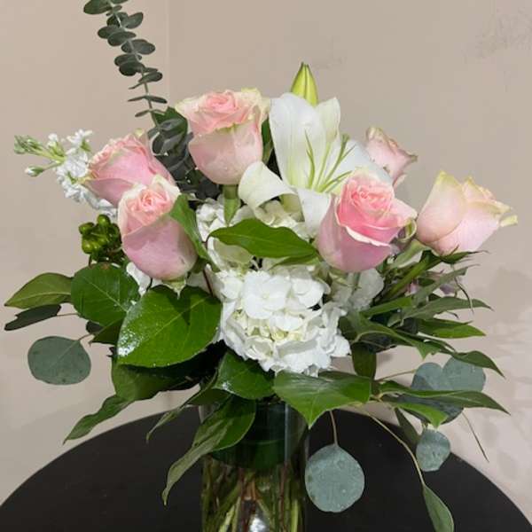 Arrangement of pink roses, white lilies, and white hydrangeas in a clear glass vase