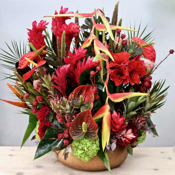 Large tropical arrangement of red and green flowers in a low gold bowl