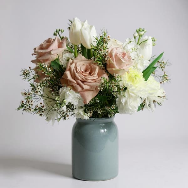 Bouquet of blush roses, white tulips, and white blooms in a blue-green vase