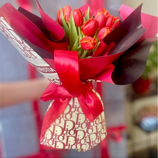 Bouquet of red tulips wrapped in pink and burgundy paper with a satin ribbon