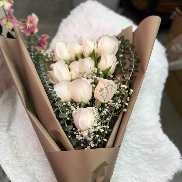 Bouquet of pale pink roses wrapped in brown paper with a white ribbon