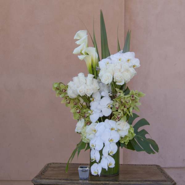 Tall white floral arrangement in a green vase with calla lilies and orchids