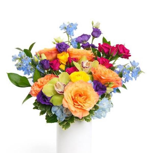 Colorful bouquet of peach roses and mixed bright blooms in a white cylinder vase