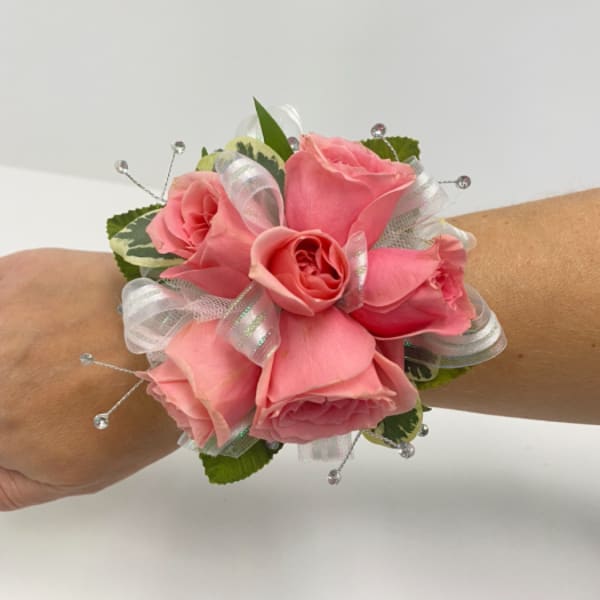 Pink rose wrist corsage with white ribbon accents and crystal bead sprays on a person's arm