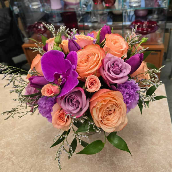 Bouquet of peach, lavender, and purple roses with orchids in a vase