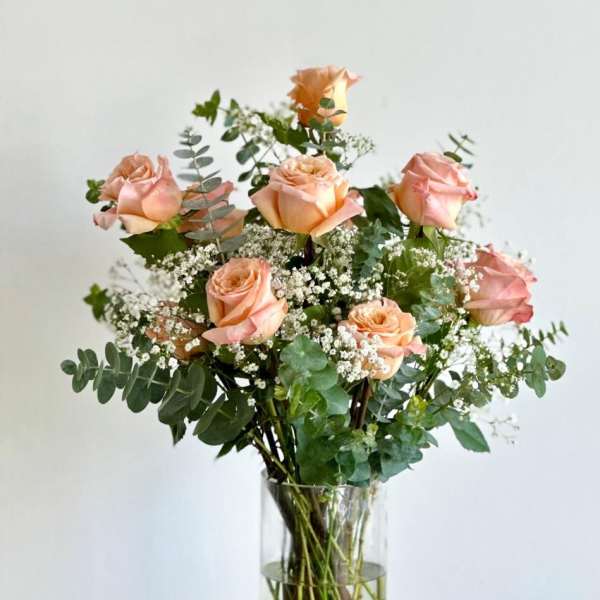 Peach roses arranged in a clear glass vase with airy white filler flowers