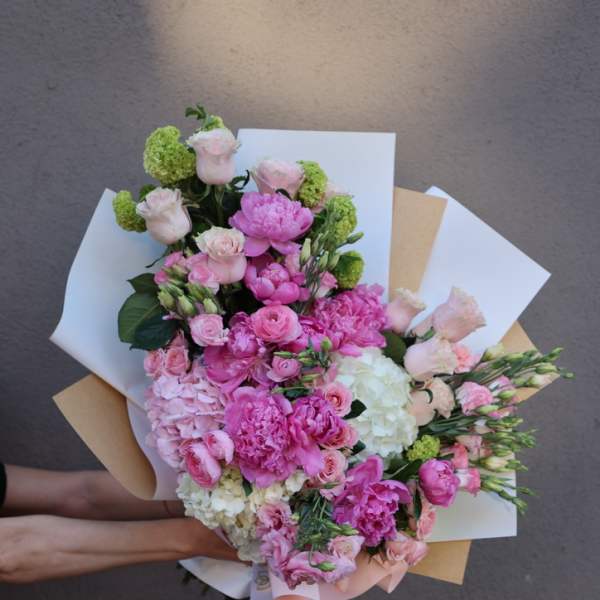 Handheld bouquet of pink and white flowers wrapped in paper